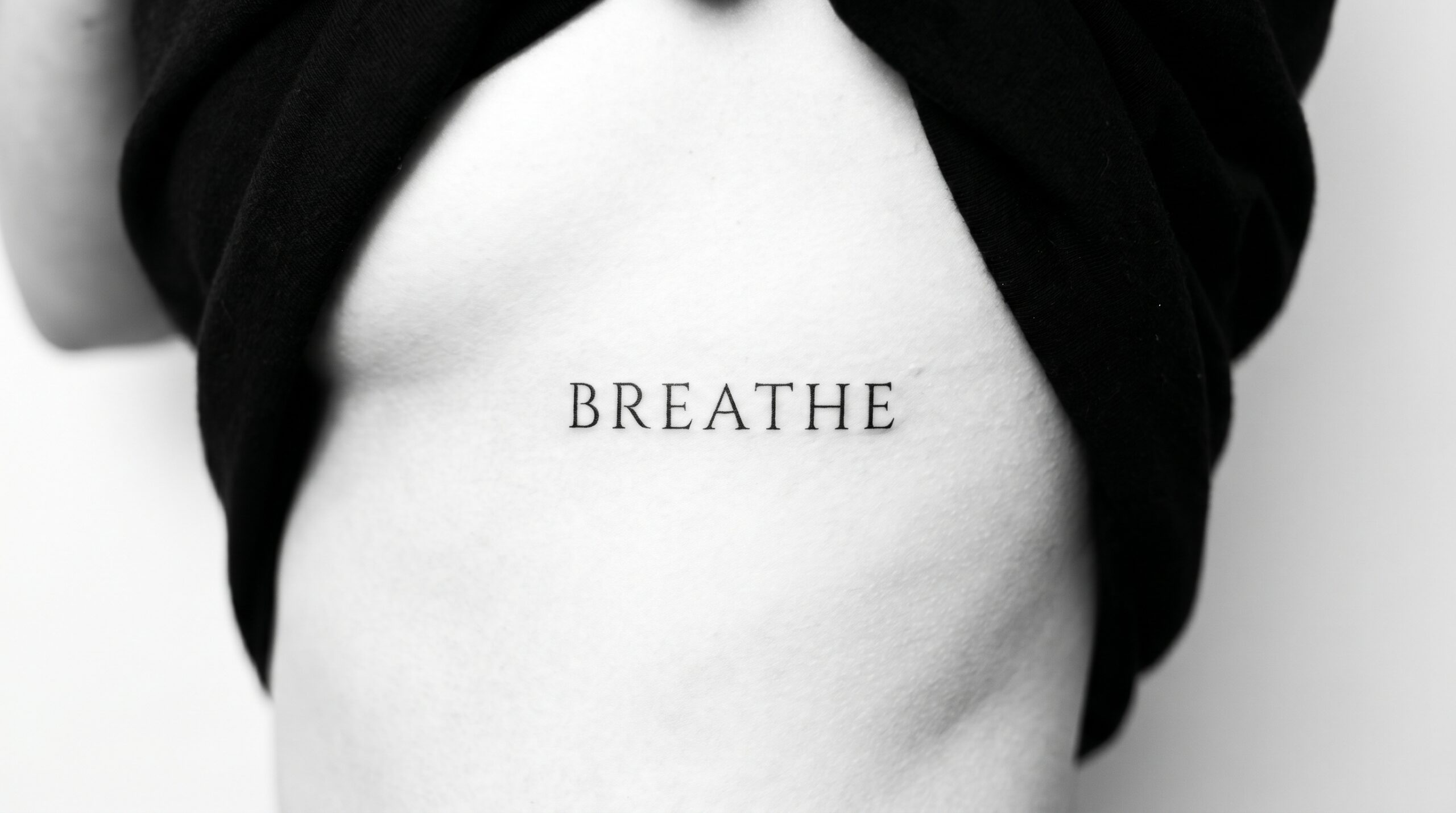 Foto ravvicinata elegante di un tatuaggio minimalista in stile script lungo la cassa toracica, con una singola parola significativa in carattere serif ultra sottile, spaziatura precisa, linee impeccabili e composizione pulita ad alto contrasto.
