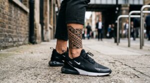 Foto professionale alla caviglia di un uomo con un vistoso tatuaggio geometrico o tribale. Indossa scarpe da ginnastica moderne e pantaloncini.